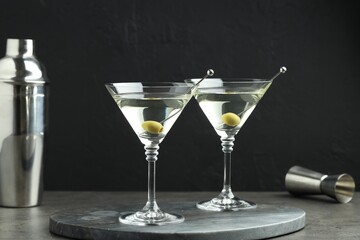 Martini cocktail with olives in glasses on grey table against black background