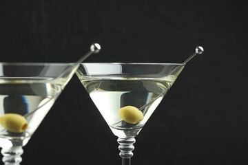 Martini cocktail with olives in glasses on black background, closeup