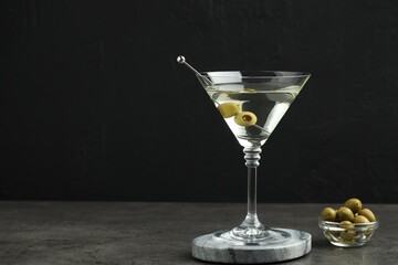 Martini cocktail with olives in glass on grey table against black background, space for text