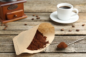Paper filter, ground coffee, grinder and cup of drink on wooden table