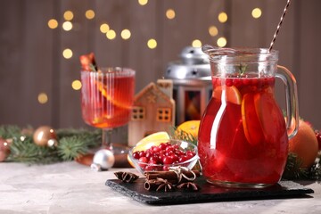 Tasty punch drink in glass jug, ingredients and Christmas decor on white table, space for text