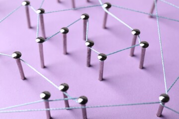 Network connection. Nails linked together by thread on violet background, closeup