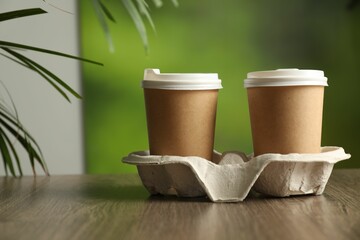 Holder with paper cups on wooden table in cafe, closeup. Mockup for design