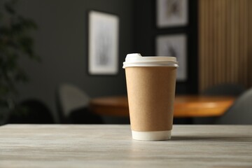 Paper cup on light wooden table in cafe. Mockup for design