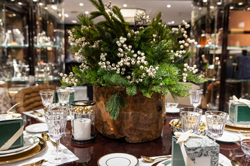 Christmas table decoration. A bouquet of spruce and fir branches with holly branches bearing white berries. Table setting includes plates, forks, knives, glasses, napkins, and wrapped gifts 