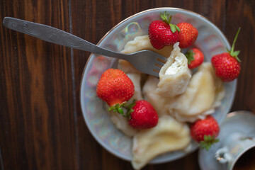 A plate of dumplings with strawberries served on a wooden table, dusted with powdered sugar. A cup of tea in a vintage porcelain cup adds a touch of elegance to this homemade meal.

