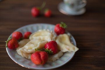 A close-up of a plate of homemade dumplings with fresh strawberries, lightly dusted with powdered sugar, placed on a dark wooden table. The warm tones create an inviting and cozy atmosphere.