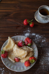 A close-up of a plate of homemade dumplings with fresh strawberries, lightly dusted with powdered sugar, placed on a dark wooden table. The warm tones create an inviting and cozy atmosphere.