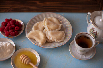 A plate of sweet dumplings with strawberries on a light blue table, with a bite taken out to reveal the creamy filling. A cup of tea sits nearby, completing the relaxing scene.
