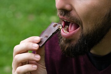 Man eating a piece of dark chocolate with nuts outdoors.