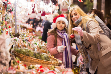 Happy mom and daughter choose christmas balls at street christmas market