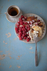 Golden-brown cottage cheese pancakes served with fresh raspberries, lightly dusted with powdered sugar. The plate is accompanied by a vintage teapot, a cup of tea, and a red gingham cloth, creating a 