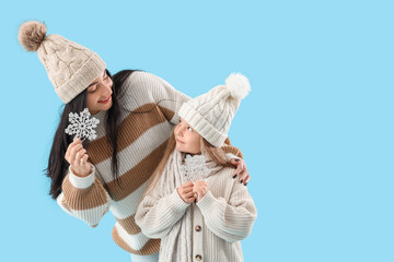 Young mother and her little daughter with snowflakes on blue background