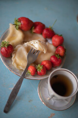 A plate of sweet dumplings with strawberries on a light blue table, with a bite taken out to reveal the creamy filling. A cup of tea sits nearby, completing the relaxing scene.
