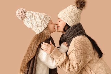 Young mother and her little daughter touching noses on beige background