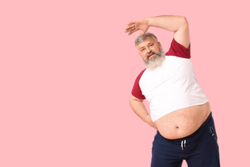 Overweight happy mature man stretching on pink background. Weight loss concept