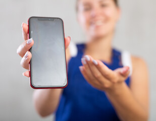 Young woman worker in overalls posing in studio with mobile phone in her hands