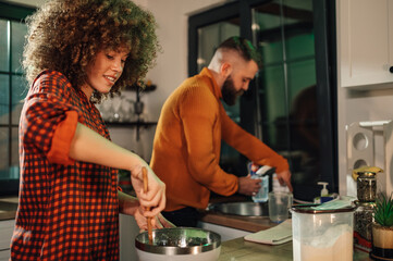 Couple cooking together in modern kitchen, woman mixing ingredients, man washing dishes