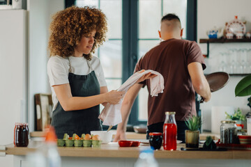 Couple cooking together in modern kitchen, preparing ingredients and using kitchen towel