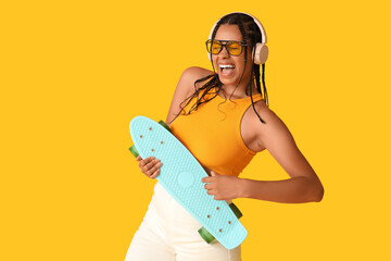 Emotional African-American woman with skateboard listening to music on yellow background