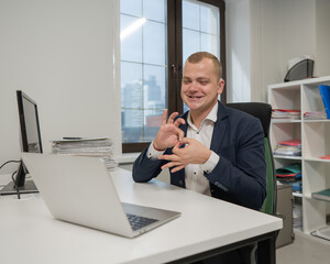 Caucasian deaf man talking sign language over video call on laptop in office.