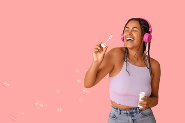 Happy African-American woman with soap bubbles listening to music on pink background