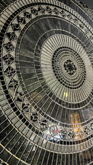 Intricate circular mosaic design featuring black, white, and silver tiles with shimmering metallic accents. Geometric patterns radiate outward in a symmetrical, detailed, and luxurious arrangement.