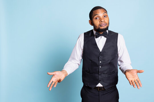 Undecided confused hotel concierge with suit and tie shrugging on camera, showing uncertainty with i dont know gesture. Clueless hotelier staff acting unsure and puzzled, confusion.