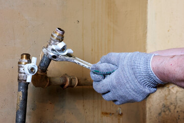 A Plumber Wearing Protective Gloves Uses A Wrench To Fix A Pipe In A Maintenance Environment. The...