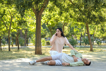 Young woman calling ambulance for man having heart attack in park © Pixel-Shot