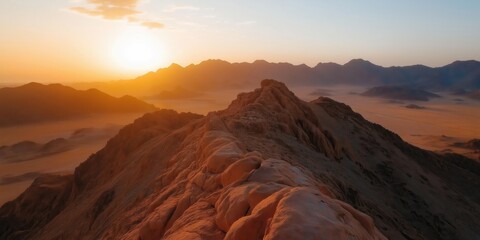 Naklejka premium A wide-angle shot of rugged, arid peaks in the Arabian Peninsula, their jagged forms highlighted by the golden hues of a setting sun