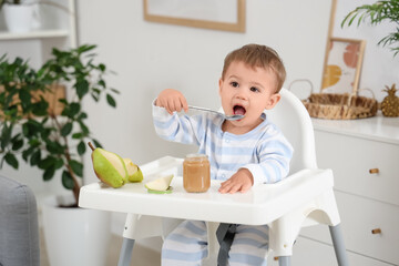 Cute little baby with jar of tasty food and fruits  eating on highchair at home