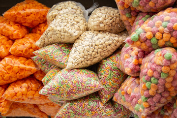 Alguns sacos plásticos com lanches industrializados;  salgadinhos, pipocas doce, cereais matinais, pendurados em exposição para venda em um comércio local.
