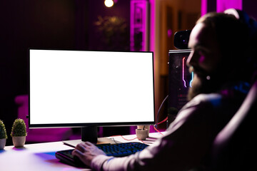 Man in dimly lit apartment playing video games on isolated screen gaming PC at computer desk,...