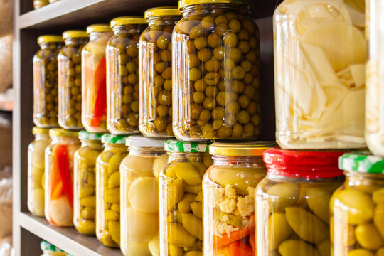 Alguns vidros com legumes em conserva, organizados em uma prateleira, em exposição para venda em um pequeno comércio local.