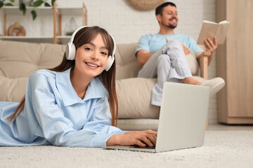 Fototapeta premium Young happy woman in pajamas with laptop and his boyfriend reading book at home