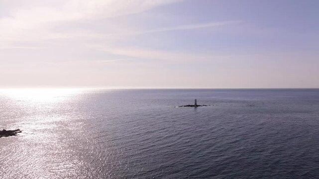 A serene Sardinian scene: Faro Mangiabarche, blue sea, white foam, and brown rocks captured by drone on a sunny day.