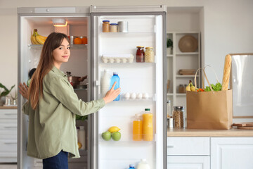 Young woman taking water bottle from open fridge in kitchen