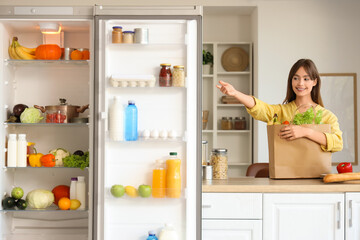 Young woman with paper bag of food on counter near open fridge in kitchen