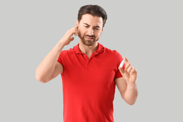 Fototapeta premium Young man with ear pain holding drops on light background