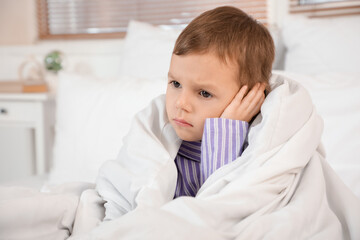 Little boy with blanket suffering from ear pain in bedroom, closeup