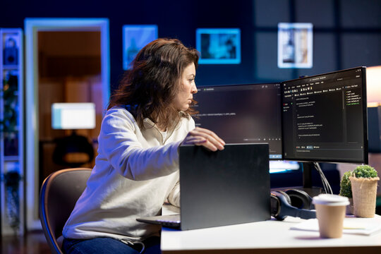 Teleworking software developer working from home opening laptop to write programs in Java programming language. Woman checking code displayed on computer screen, sitting at desk chair