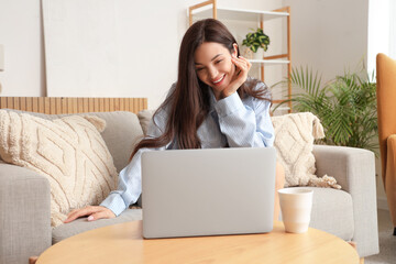 Fototapeta premium Young woman in blue pajamas working with laptop at home