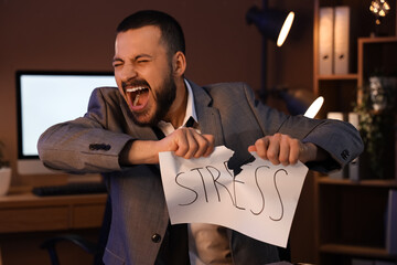 Angry businessman tearing paper with word STRESS in office at night
