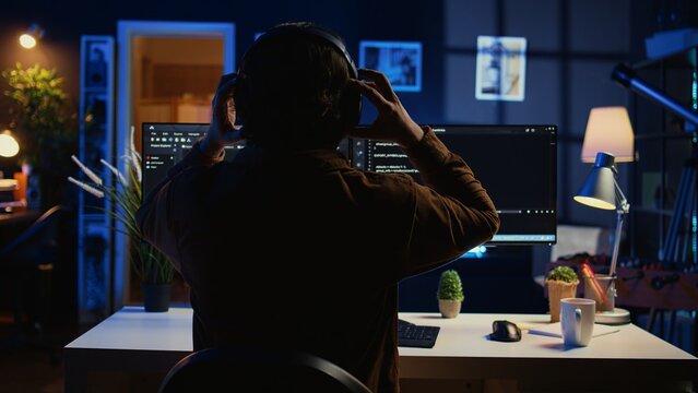 Technician putting headphones on while using coding to fortify firewalls, teleworking for IT company. Computer scientist listening music and upgrading binary code scripts in home office, camera B