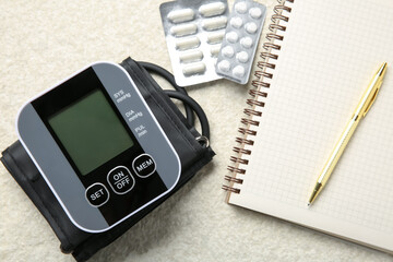 Blood pressure measuring device, pills and notebook on light textured background, top view