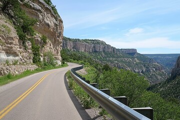 Mountain road curves through canyon, guardrail present.