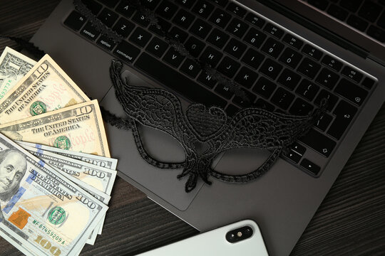 Sex work. Laptop, mask, smartphone and money on wooden surface, closeup - Powered by Adobe