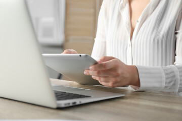 Businesswoman using tablet at wooden table indoors, closeup. Modern technology