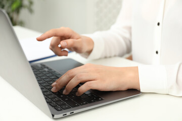 Businesswoman using laptop at white table indoors, closeup. Modern technology